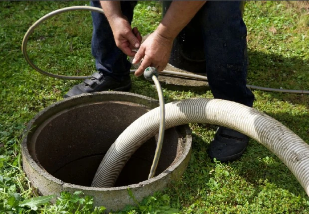 Technician guiding a hose into a septic tank for maintenance service