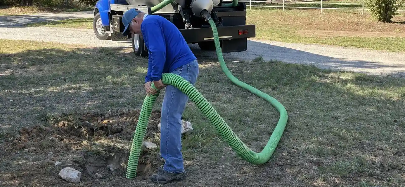 Technician using a large vacuum hose for professional septic tank pumping.